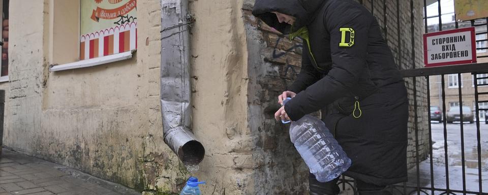 Une ukrainienne récupère l'eau de pluie d'une gouttière. [Keystone/AP Photo - John Leicester]