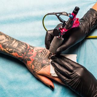 Une tatoueuse tattoo un client. [Depositphotos - ivanriver]