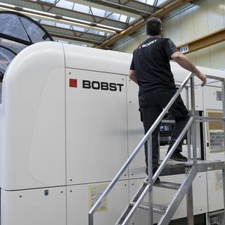 Un employé de l'entreprise Bobst devant une machine de découpe de carton. [Keystone - Jean-Christophe Bott]