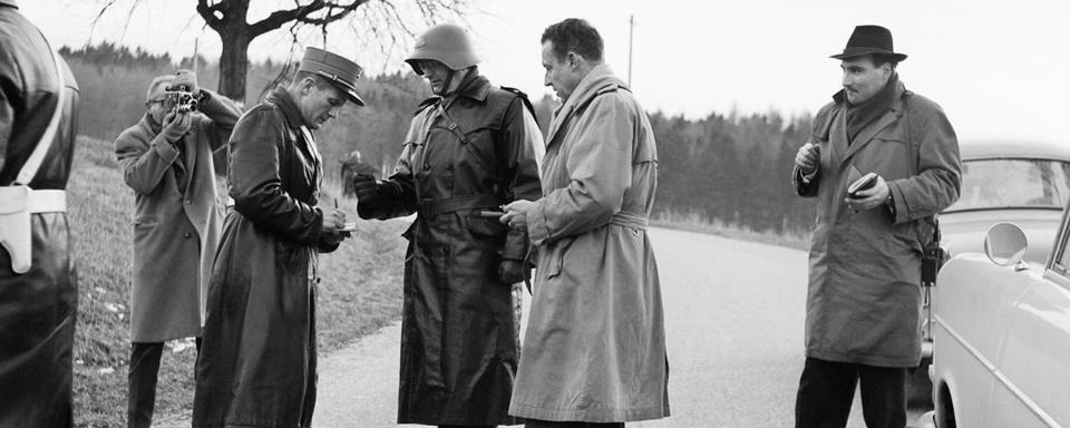 En mars 1962, policiers et militaires suisses contrôlent la route d'accès à l'hôtel "Les Horizons Bleus" près du Signal de Bougy au-dessus de Rolle (VD), où la délégation algérienne est hébergée durant la conférence sur l'Algérie. Le 18 mars de cette même année, la conférence entre l'Algérie et la France, puissance coloniale, aboutira à la signature d'un accord mettant fin à la longue guerre d'indépendance qui avait commencé en 1954 entre ces deux pays. [Keystone / Photopress-Archiv/Str]