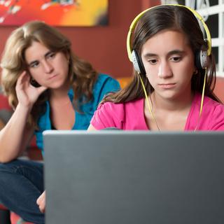 Une mère regarde sa fille jouer sur son ordinateur d'un air désapprobateur. [Depositphotos - kmiragaya]