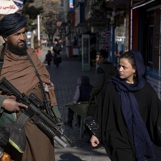 Une femme afghane passe à côté d'un taliban dans une rue de Kabul. [AP Photo/Keystone - Ebrahim Noroozi]