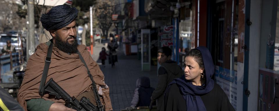 Une femme afghane passe à côté d'un taliban dans une rue de Kabul. [AP Photo/Keystone - Ebrahim Noroozi]