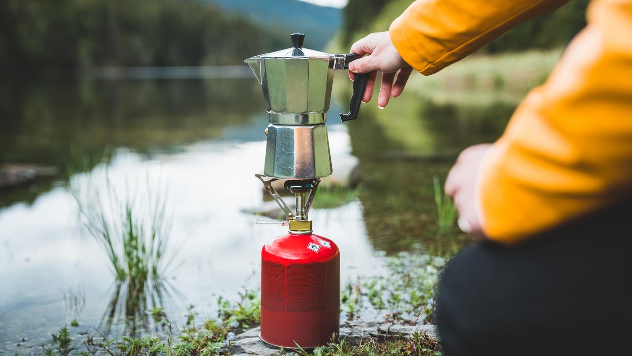 Un réchaud de camping et une cafetière au bord d'un lac. [Depositphotos - Claudiumaxim]