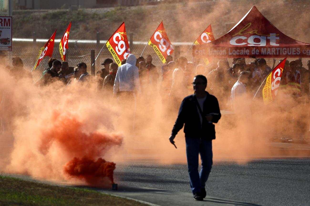 Des travailleurs de TotalEnergies et d'Esso ExxonMobil lâchent des fumigènes lors d'une manifestation à l'appel du syndicat CGT devant la raffinerie TotalEnergies de La Mede, le 11 octobre. [Keystone - GUILLAUME HORCAJUELO]