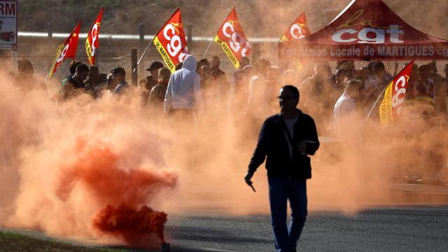 Des travailleurs de TotalEnergies et d'Esso ExxonMobil lâchent des fumigènes lors d'une manifestation à l'appel du syndicat CGT devant la raffinerie TotalEnergies de La Mede, le 11 octobre. [Keystone - GUILLAUME HORCAJUELO]