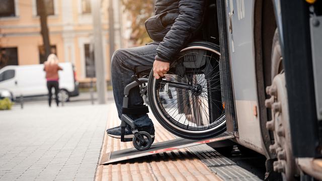 Une homme avec une handicap physique descend d'un bus sur une rampe d'accès pour fauteuil roulant. [Depositphotos - Romaset]