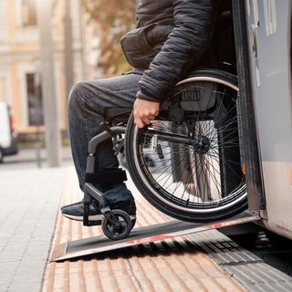 Une homme avec une handicap physique descend d'un bus sur une rampe d'accès pour fauteuil roulant. [Depositphotos - Romaset]