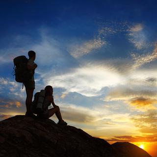 Deux personnes admirent le coucher de soleil au sommet d'une montagne. [Depositphotos - mihtiander]