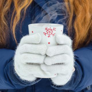 Une femme avec des gants tient une tasse de thé chaud dehors dans la neige. [Depositphotos - umkaLETO]
