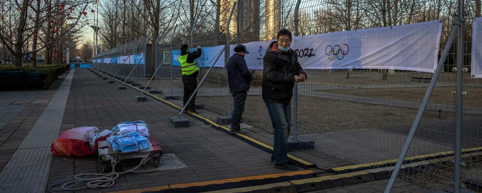 Des volontaires attachent des banderoles sur des barrières à proximité du site olympique à Pékin. [Keystone/EPA - Roman Pilipey]