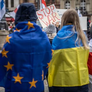 Deux participantes à une marche pour la paix se tiennent debout, enveloppées dans un drapeau de l'UE (à gauche) et un drapeau ukrainien (à droite), tandis qu'une pancarte portant l'inscription "Stop War" est tenue en arrière-plan, le 2 avril 2022 à Hesse, Francfort-sur-Main. [KEYSTONE/DPA - Frank Rumpenhorst]