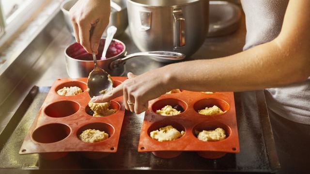 Une personne place de petites portions de pâte à gâteau avec une cuillère dans des moules en silicone (image d'illustration). [AFP - Mint Images]