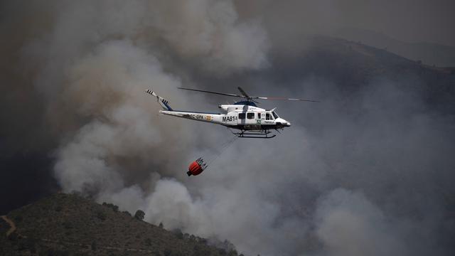 Un hélicoptère tentant de contenir un incendie dans la montagne de la Sierra Bermeja, dans la province de Málaga en Espagne, est photographié depuis Benahavís, le 9 juin 2022. [AFP - Jorge Guerrero]