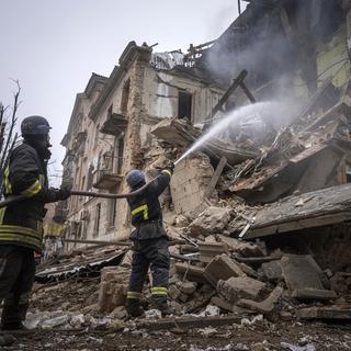 Les pompiers ukrainiens tentent d'éteindre un bâtiment en feu après une attaque de missiles russes. [AP Photo/Keystone - Evgeniy Maloletka]