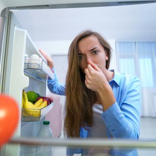 Une femme se pince le nez en ouvrant son frigo. [Depositphotos - goffkein]