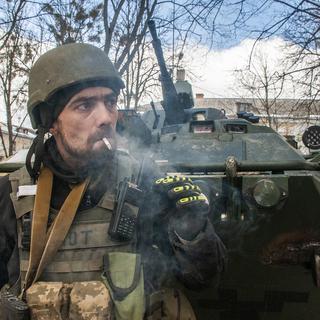 Un volontaire des forces de défense territoriale ukrainiennes se tient à côté de son APC à Kharkiv, en Ukraine, le mercredi 16 mars 2022. [AP Photo/KEYSTONE - Andrew Marienko]
