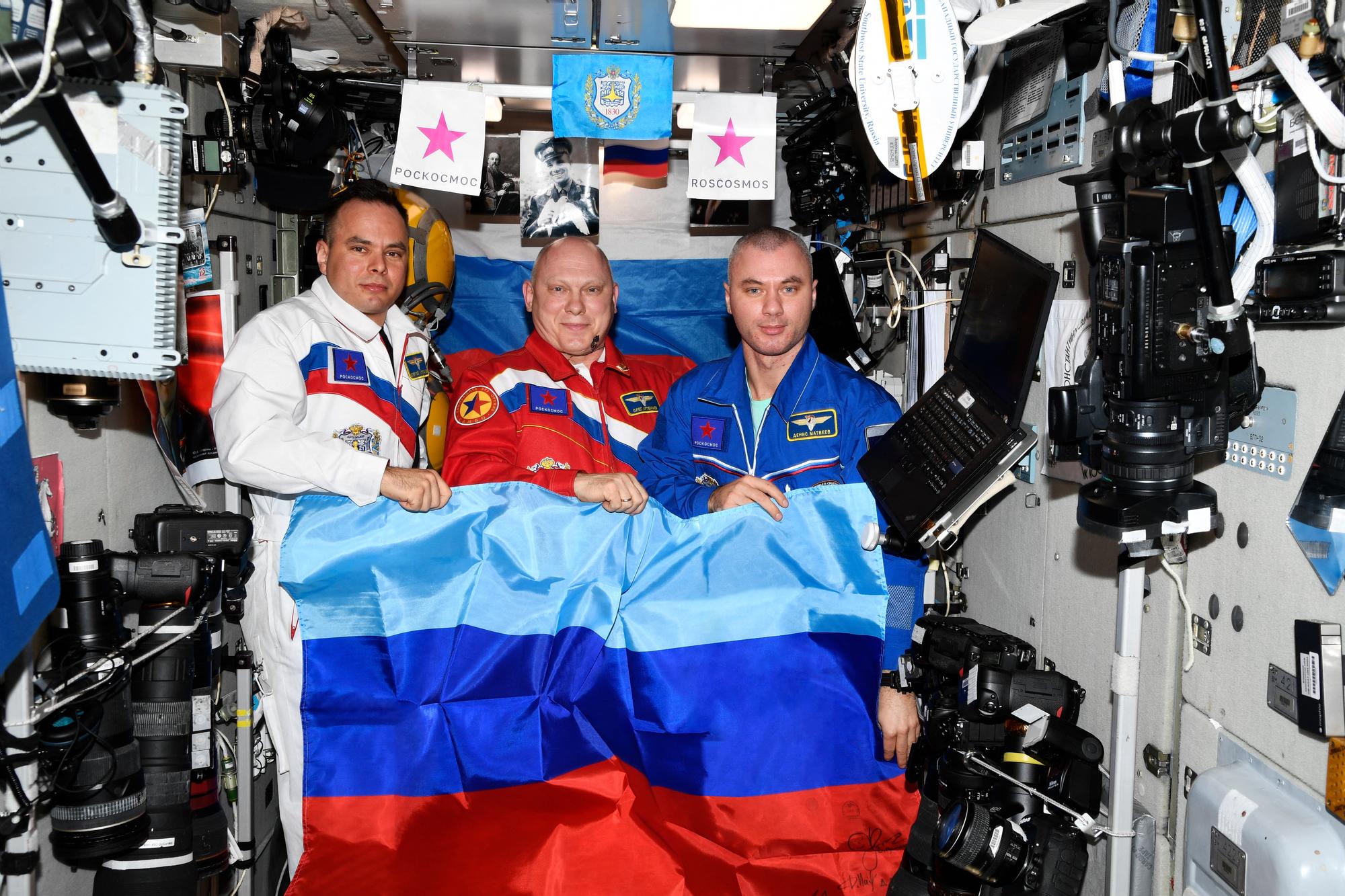 Les cosmonautes russes Sergei Korsakov, Oleg Artemyev et Denis Matveyev posent avec un drapeau de la République populaire autoproclamée de Lougansk à bord de la Station spatiale internationale (ISS). [AFP - Roscosmos]