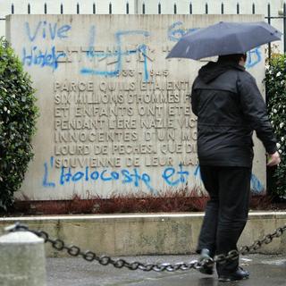 Une personne passe devant plusieurs croix gammées et des inscriptions antisémites  taguées sur la grande synagogue Beth Yaacov de Genève. [KEYSTONE - Martial Trezzini]