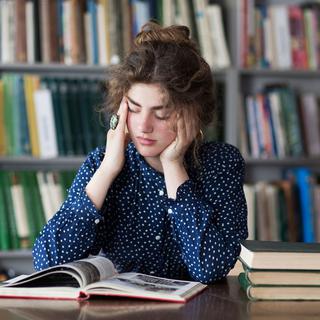 Une étudiante a l'air exténuée en lisant des livres dans une bibliothèque. [Depositphotos - alin.s]