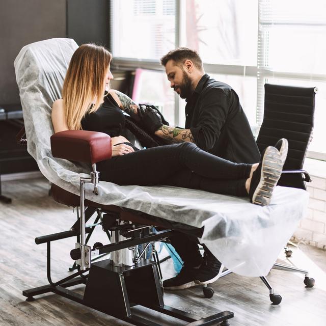 Jeune femme en train de se faire tatouer dans un salon de tatouage. [Depositphotos - Garetsworkshop]