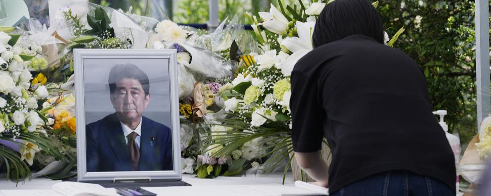 Une femme écrit un message après avoir déposé un bouquet de fleurs pour l'ancien Premier ministre japonais assassiné Shinzo Abe, le 11 juillet 2022 à Tokyo. [KEYSTONE - Hiro Komae / AP Photo]