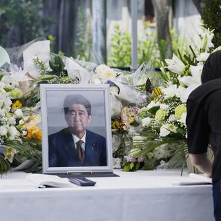 Une femme écrit un message après avoir déposé un bouquet de fleurs pour l'ancien Premier ministre japonais assassiné Shinzo Abe, le 11 juillet 2022 à Tokyo. [KEYSTONE - Hiro Komae / AP Photo]