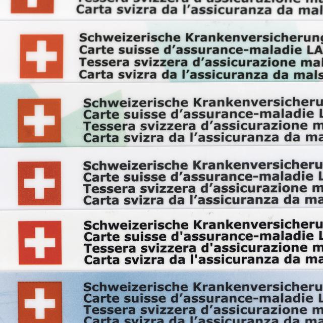 Plusieurs cartes d'assurance maladie en Suisse empilées. [Keystone - Christian Beutler]