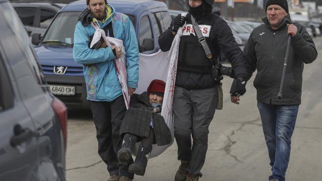 Des habitants et un journaliste aident une femme âgée à fuir la ville d'Irpin, située sur la ligne de front, dans la région de Kiev, en Ukraine, le 9 mars 2022 [EPA/STRINGER]