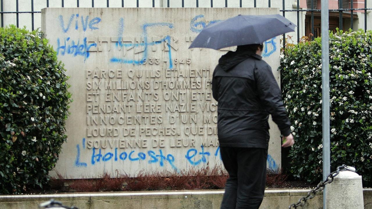 Une personne passe devant plusieurs croix gammées et des inscriptions antisémites  taguées sur la grande synagogue Beth Yaacov de Genève. [KEYSTONE - Martial Trezzini]