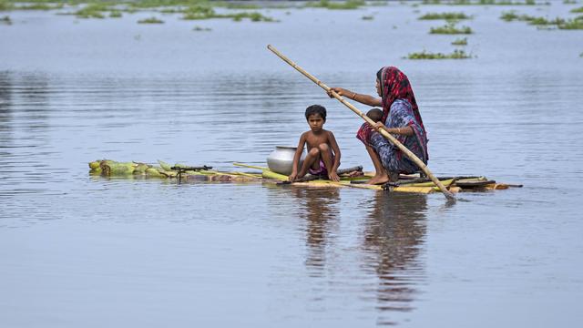 Une femme accompagnée d'un enfant rame sur un radeau de fortune après d'importantes inondations, dans le village de Tarabari de l'État indien d'Assam, au nord-est du pays. [KEYSTONE - Anupam Nath / AP Photo]