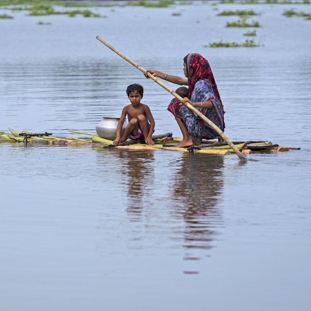Une femme accompagnée d'un enfant rame sur un radeau de fortune après d'importantes inondations, dans le village de Tarabari de l'État indien d'Assam, au nord-est du pays. [KEYSTONE - Anupam Nath / AP Photo]