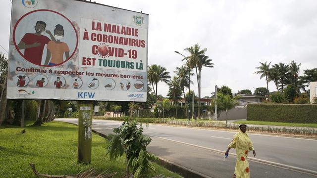 Une femme passe devant un panneau affichant un message de sensibilisation au COVID-19 en français, indiquant "La maladie à coronavirus (COVID-19) est toujours là. Continuez à respecter les mesures de barrières", à Abidjan, Côte d'Ivoire, le 5 août 2021. [EPA/KEYSTONE - LEGNAN KOULAKOULA]