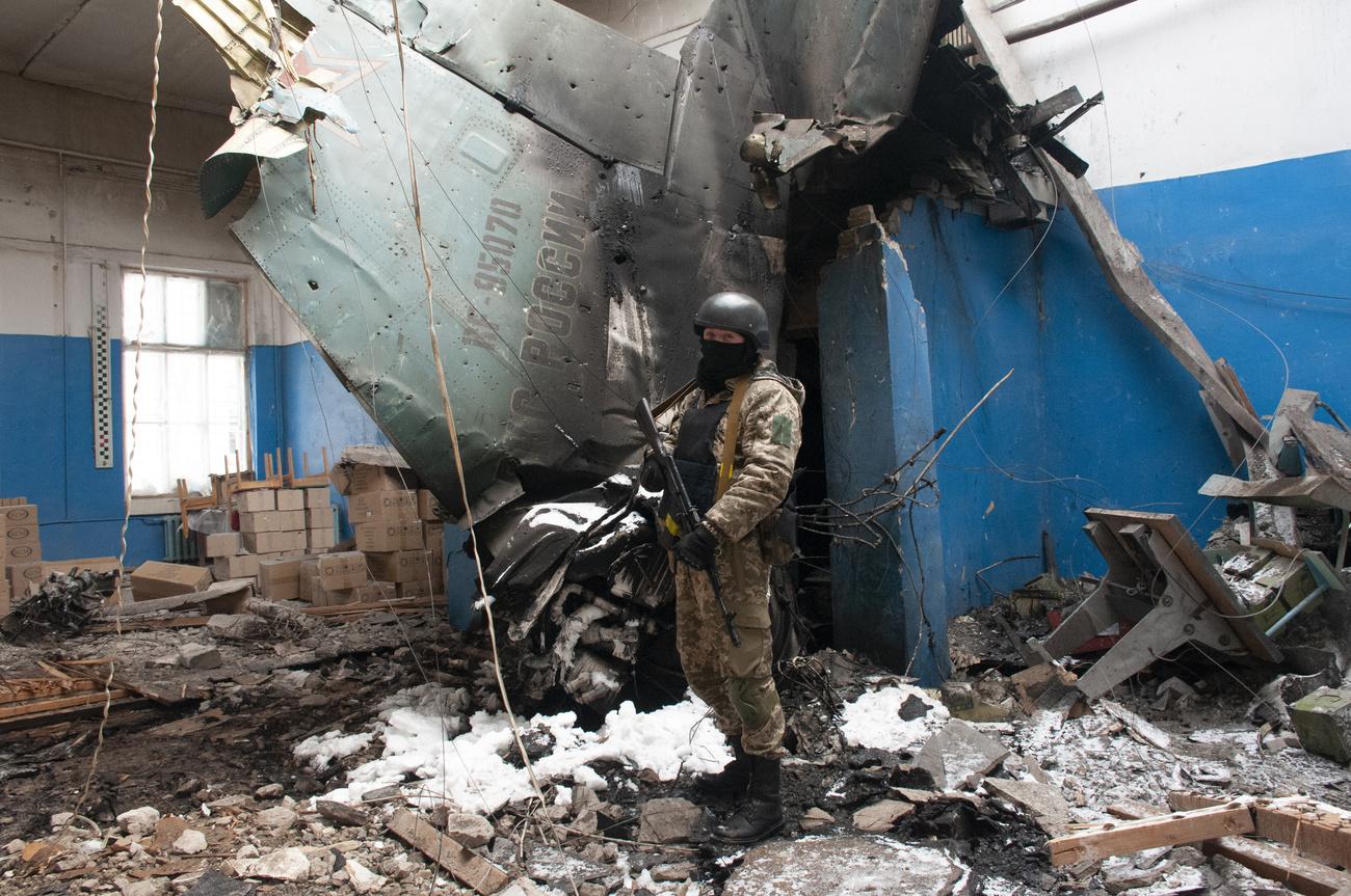 Un soldat ukrainien devant les débris d'un avion russe Su-34 dans la ville de Kharkiv, le 8 mars 2022. [Keystone - Andrew Marienko]