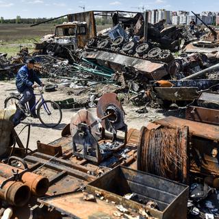 Un homme passe à vélo devant des débris dans une casse à Bucha, en Ukraine, le 10 mai 2022. [EPA/KEYSTONE - Oleg Petrasyuk]