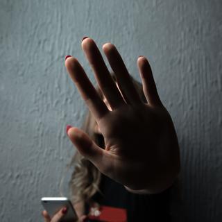 Une femme tenant un téléphone portable dit 'stop' de la main. [Depositphotos - Burdun]
