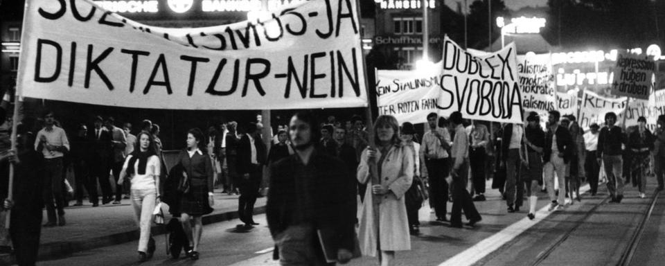 Manifestation contre l'invasion de la Tchécoslovaquie par les troupes soviétiques et la répression brutale du "Printemps de Prague" dans le quartier de la gare à Zurich, fin août 1968. Sur la première banderole on peut lire "Oui au socialisme, non à la dictature". -Avec l'arrivée au pouvoir du réformateur Alexander Dubček en janvier 1968, le Parti communiste tchécoslovaque introduit le "socialisme à visage humain" et prône une relative libéralisation. Ce mouvement s'achève le 21 août 1968 avec l'invasion du pays par les troupes du Pacte de Varsovie. [KEYSTONE/Str]