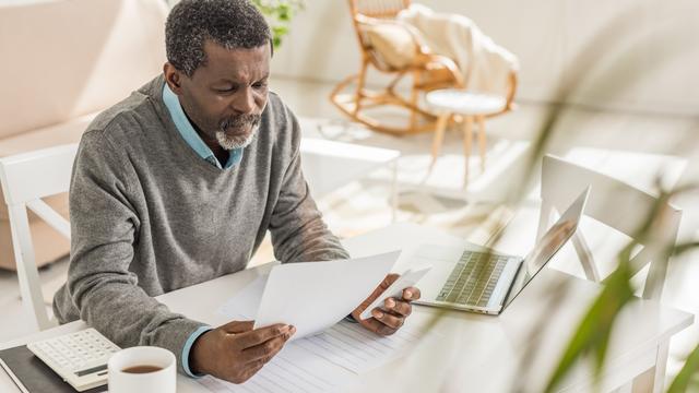 Un homme est assis à une table et analyse des documents. [Depositphotos - AndrewLozovyi]