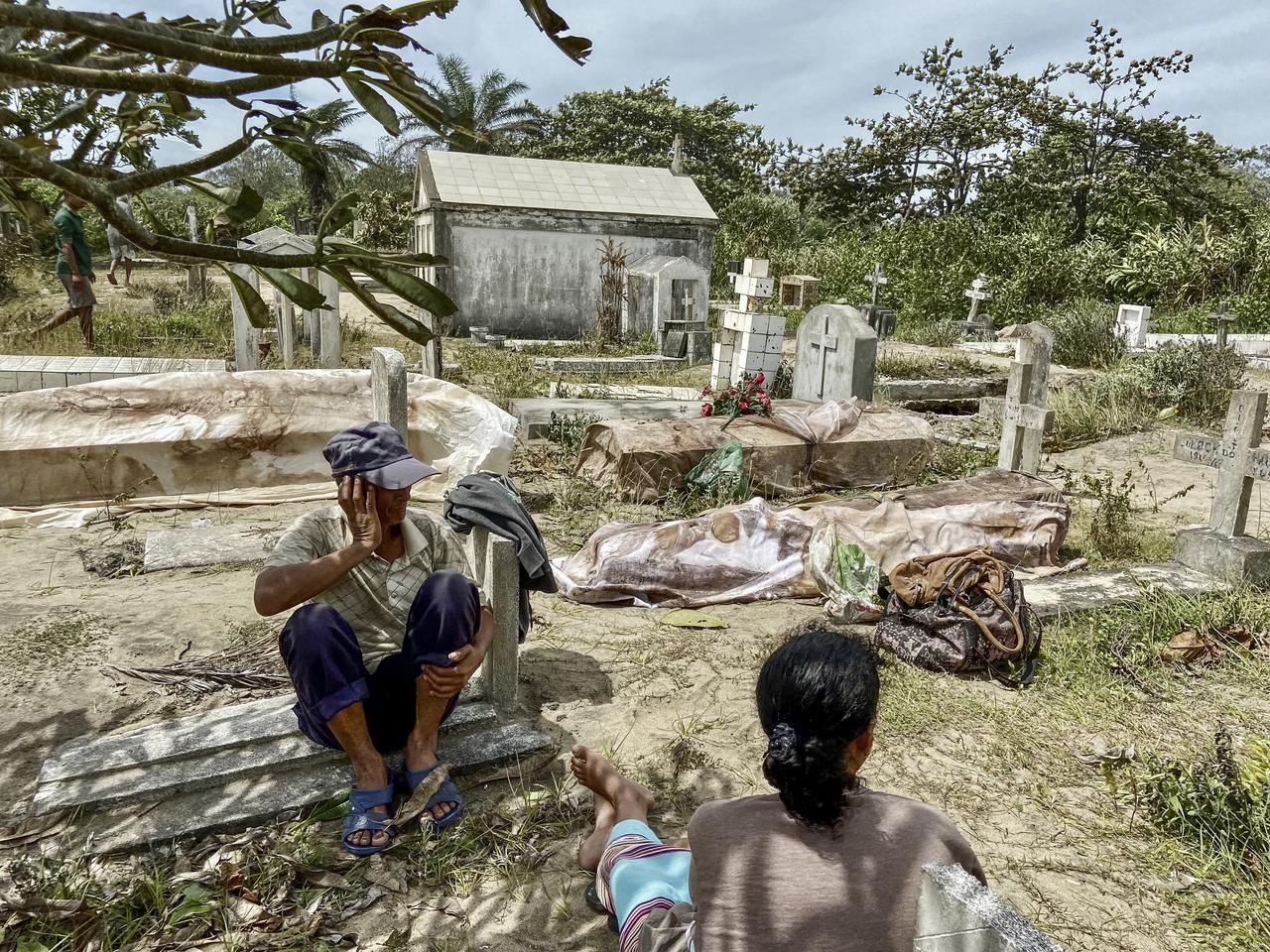 Des proches sont assis à côté des corps exhumés des tombes détruites par le cyclone Batsirai au cimetière local de Mahanoro. [AFP - Laure Verneau]