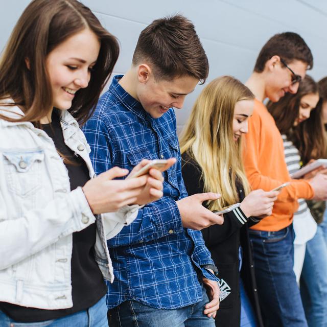 Six adolescents et adolescentes adossés à un mur consultent leur smartphone. [Depositphotos - anatoliycherkas]