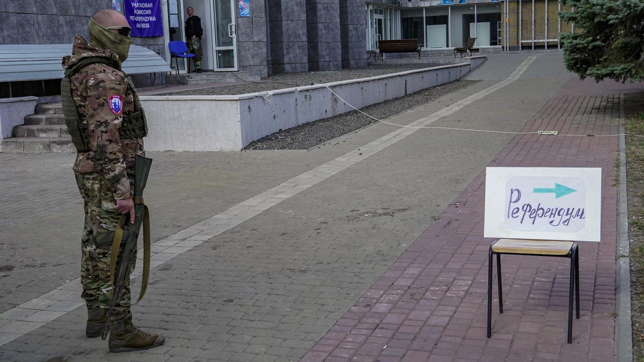 Un militaire russe monte la garde près d'un panneau indiquant "Référendum" à Marioupol le 25 septembre 2022. [Keystone/EPA - Stringer]