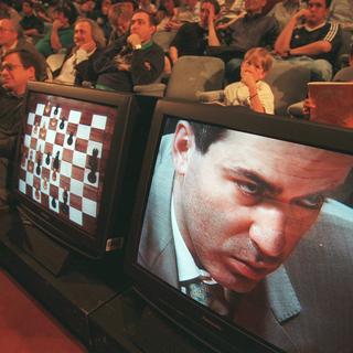 JUn public regarde Garry Kasparov sur un écran de télévision en train de réfléchir à son prochain coup contre Deep Blue, l'ordinateur d'échecs d'IBM, lors de la première partie de leur match revanche de six matchs, samedi 3 avril 1997, à New York. [KEYSTONE/AP - AdamNadel]