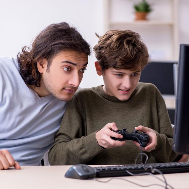 Un père regarde l'écran de son fils en train de jouer à un jeu vidéo. [Depositphotos - Elnur_]