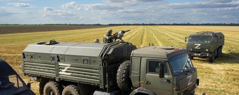 Un soldat russe au sommet d'un camion militaire portant la lettre Z, devenue le symbole de l'armée russe, et un hashtag "Nous n'abandonnons pas les nôtres" surveille une zone pendant que des journalistes étrangers observent et filment les agriculteurs de la ferme Voznesenka-Agro qui récoltent avec leur moissonneuse-batteuse dans un champ de blé non loin de Melitopol, dans le sud de l'Ukraine, jeudi 14 juillet 2022. [Photo AP/KEYSTONE]