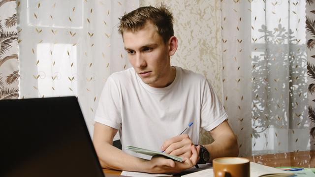 Un jeune homme regarde son ordinateur et prend des notes. [Depositphotos - bo.kvk]