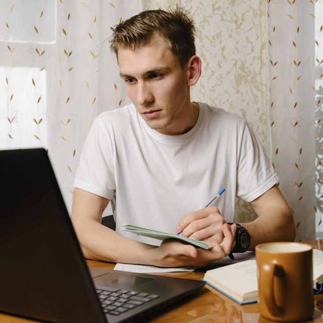 Un jeune homme regarde son ordinateur et prend des notes. [Depositphotos - bo.kvk]