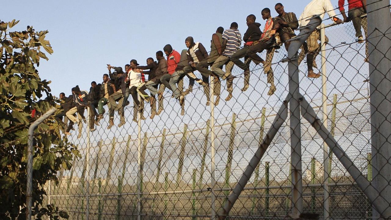 Des migrants sont assis au sommet d'une clôture alors qu'ils tentent de rejoindre Melilla, l'exclave espagnole sur la côte nord-africaine, le 22 octobre 2014. [EPA/KEYSTONE - Francisco G. Guerrero]