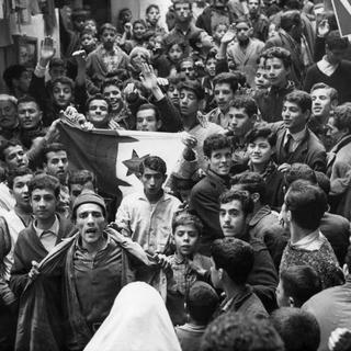 Après l'annonce du cessez-le-feu le 19 mars 1962 entre l'Algérie et la France, de jeunes musulmans défilent dans le vieux quartier de la Casbah à Alger, en Algérie, avec un drapeau vert et blanc, photographié le 21 mars 1962. [(KEYSTONE/Str)]