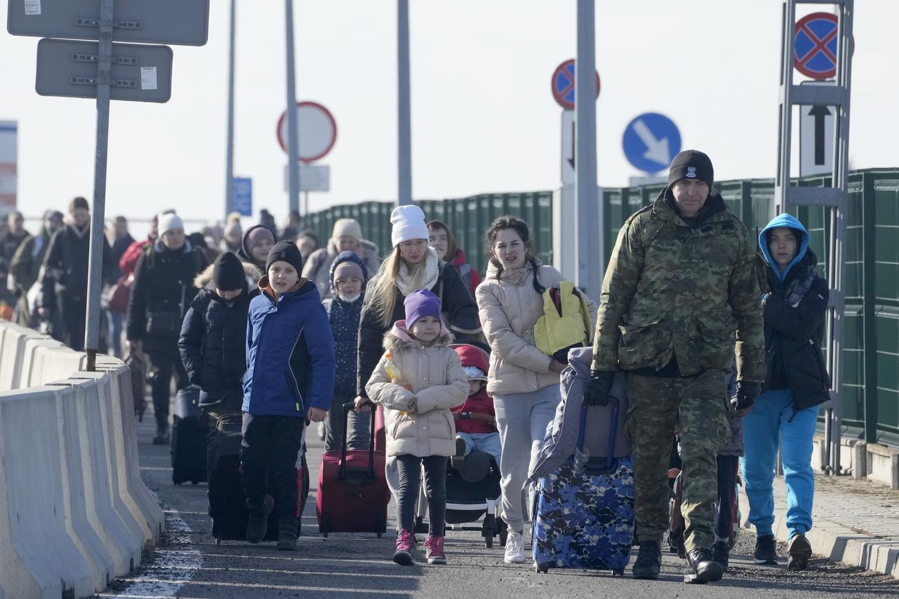 Un garde-frontière aidant des réfugiés ukrainiens arrivant à la frontière polonaise. [AP Photo/Keystone - Czarek Sokolowski]