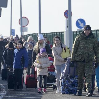 Un garde-frontière aidant des réfugiés ukrainiens arrivant à la frontière polonaise. [AP Photo/Keystone - Czarek Sokolowski]
